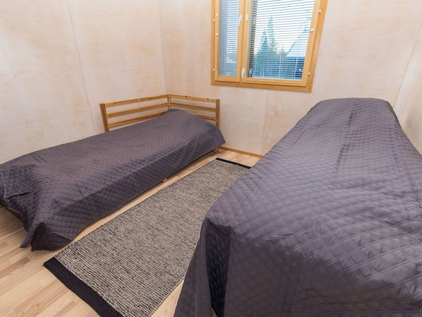Un alojamiento pequeño y con una sola habitación, con dos camas individuales, una ventana con persianas y una alfombra estampada en el suelo.