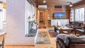 A cozy cabin interior with a fireplace, wooden flooring, a sofa, and a television. - Teknomaja by Interhome (Äkäslompolo)