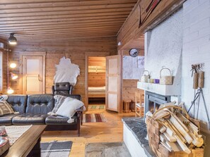 A cozy log cabin interior with a leather sofa, a fireplace, and a rustic wooden ceiling.