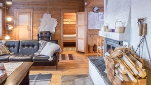 A cozy cabin interior with a leather sofa, a wooden dining table, a fireplace, and a stone wall. - Teknomaja by Interhome (Äkäslompolo)