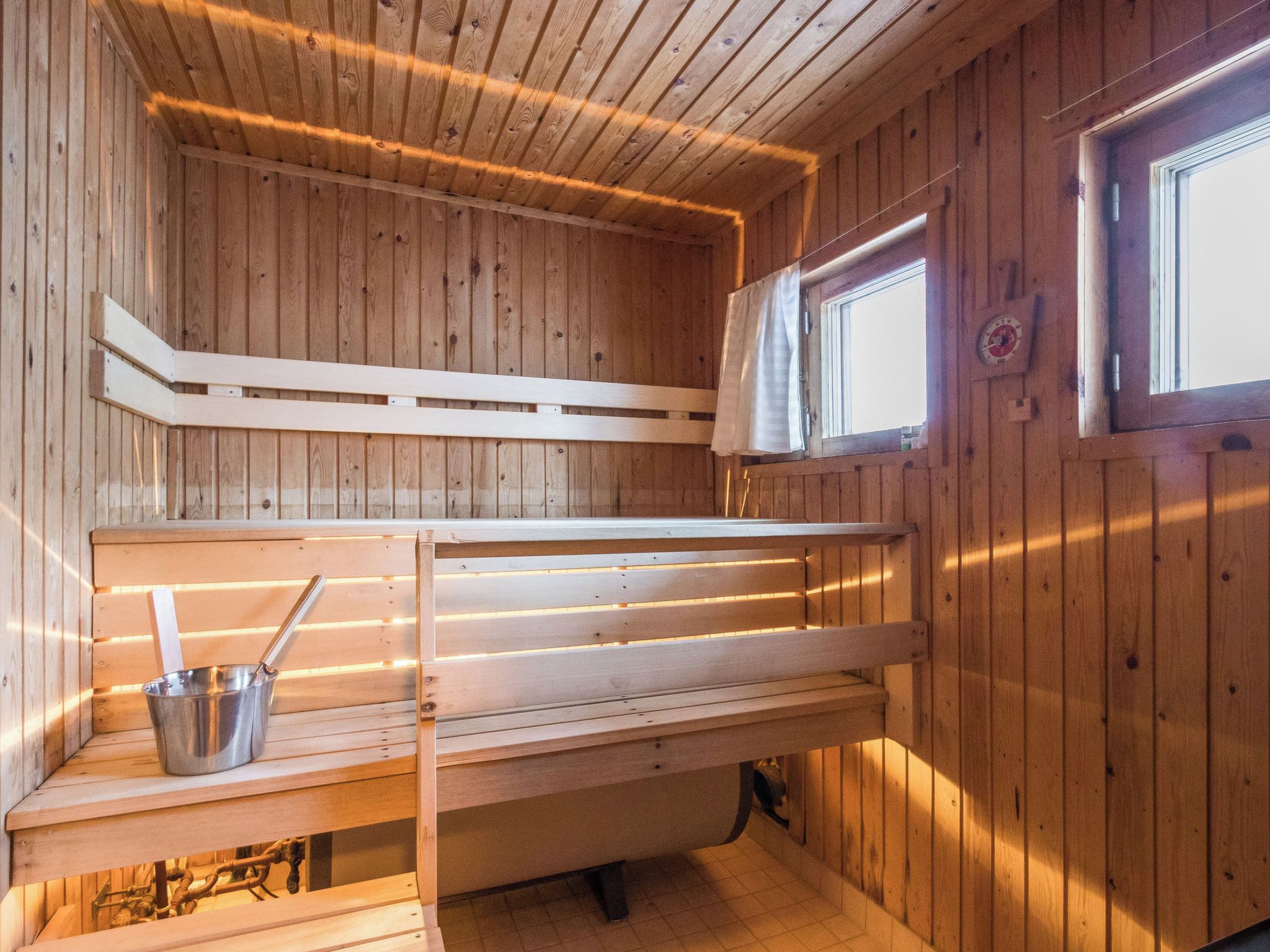 Un sauna con paredes de madera, un banco, una ventana y un cubo de metal.