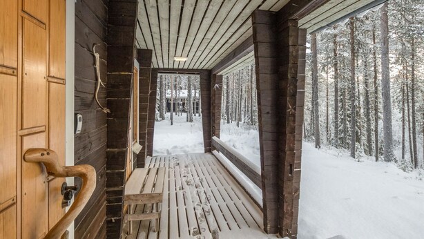 A wooden cabin with a snow-covered deck and a view of a snowy forest. - Teknomaja by Interhome (Äkäslompolo)