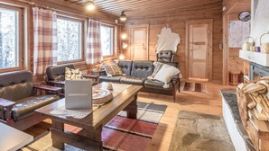 A cozy cabin interior with wooden walls, a leather sofa, a wooden coffee table, and a fireplace. - Teknomaja by Interhome (Äkäslompolo)