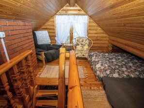 A cozy attic bedroom with a sloped ceiling, a brick wall, a wooden bench, a floral-patterned bed, and a wicker chair.