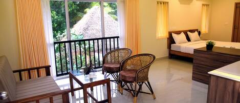 A hotel room with a balcony, a bed, a dining table with chairs, and a small potted plant.