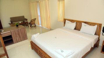 A hotel room with a bed, a desk, a chair, a ceiling fan, and curtains.