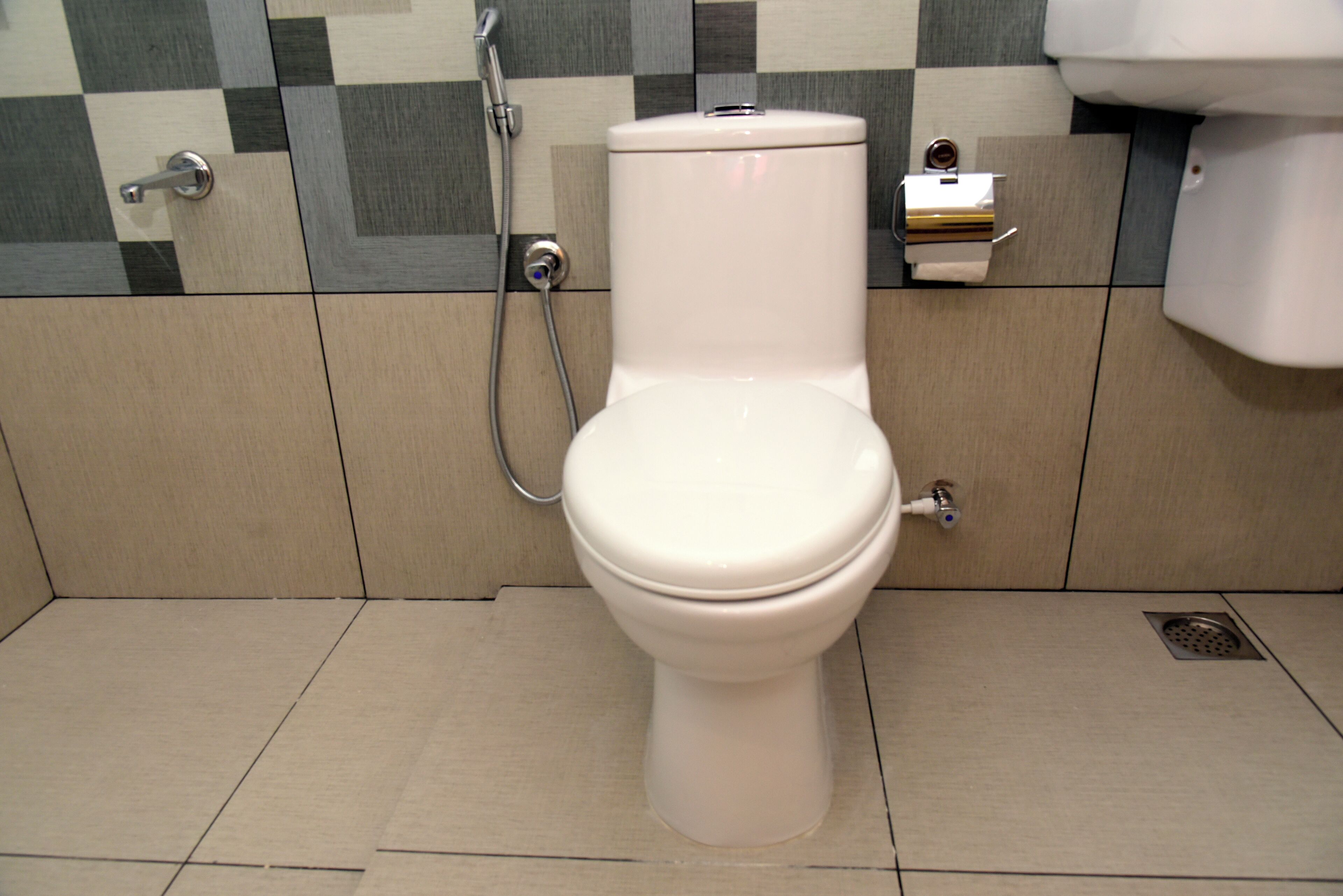 A toilet with a bidet attachment in a bathroom with checkered tile walls and a tiled floor.