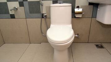 A toilet with a bidet attachment in a bathroom with checkered tile walls and a tiled floor.