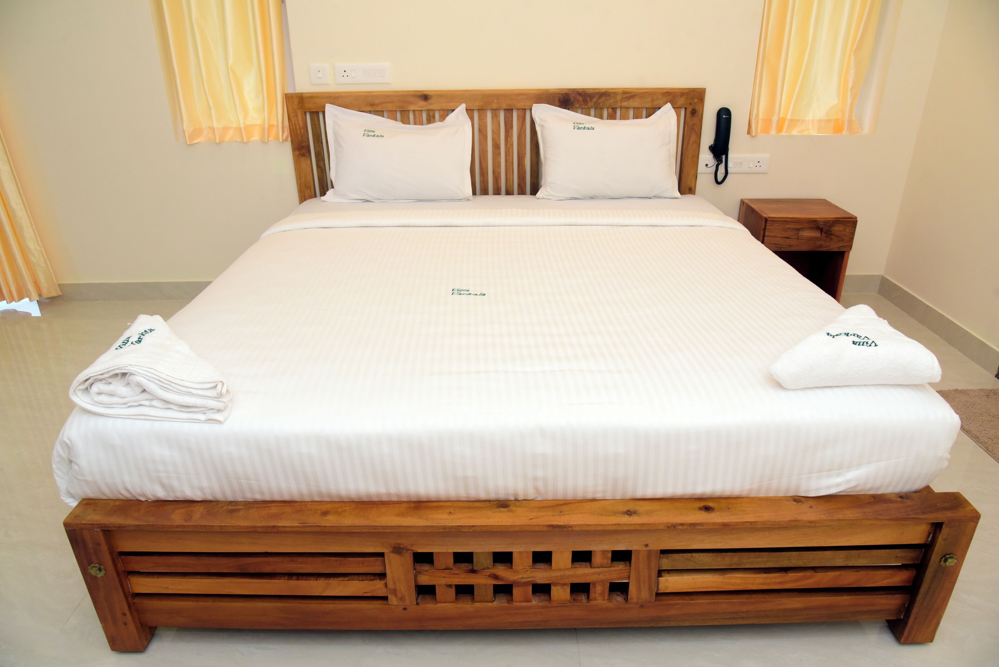 A neatly made bed with a wooden frame, white bedding, and a small bedside table with a phone.