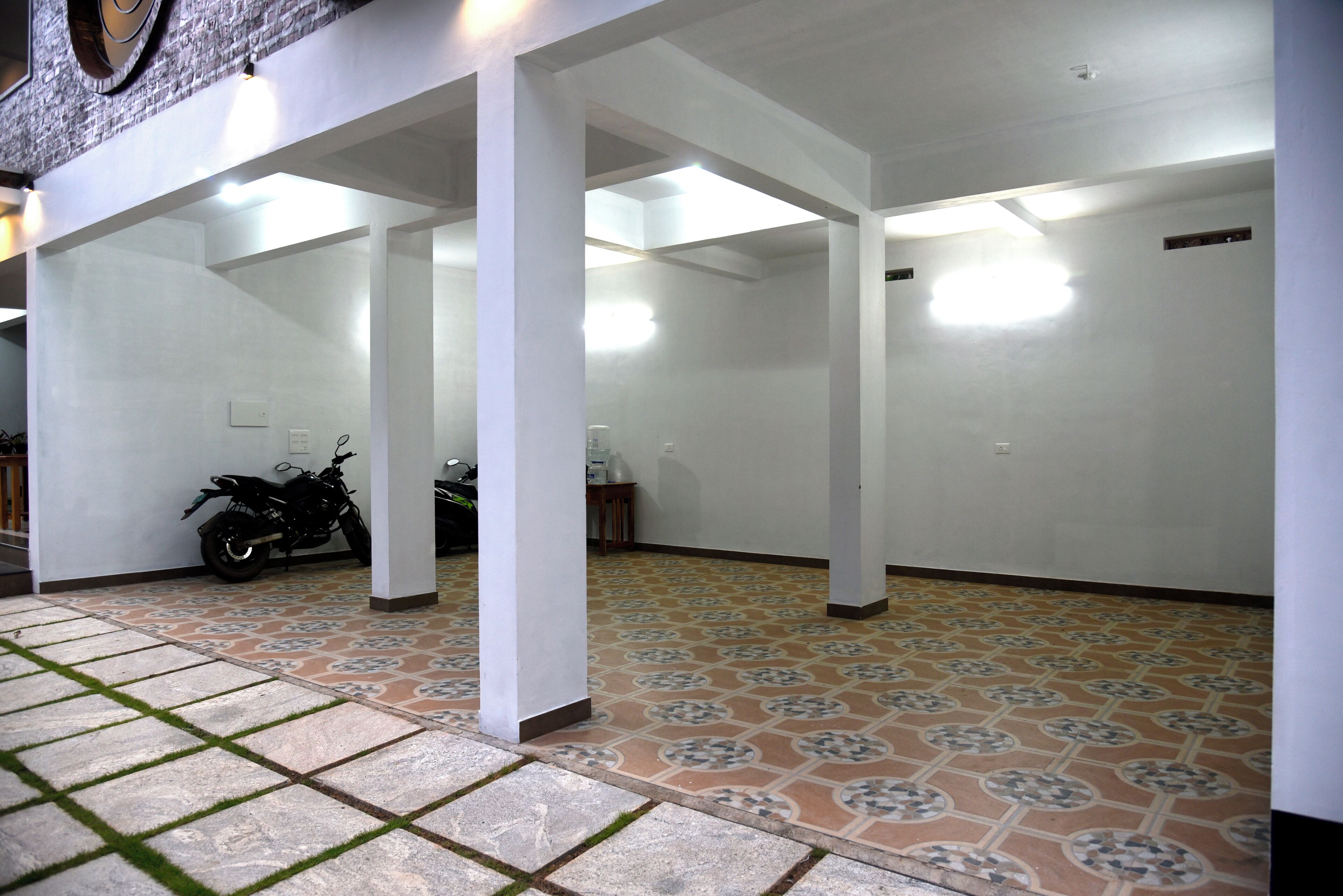 A covered outdoor area with tiled flooring, white pillars, and a motorcycle parked under a shelter.