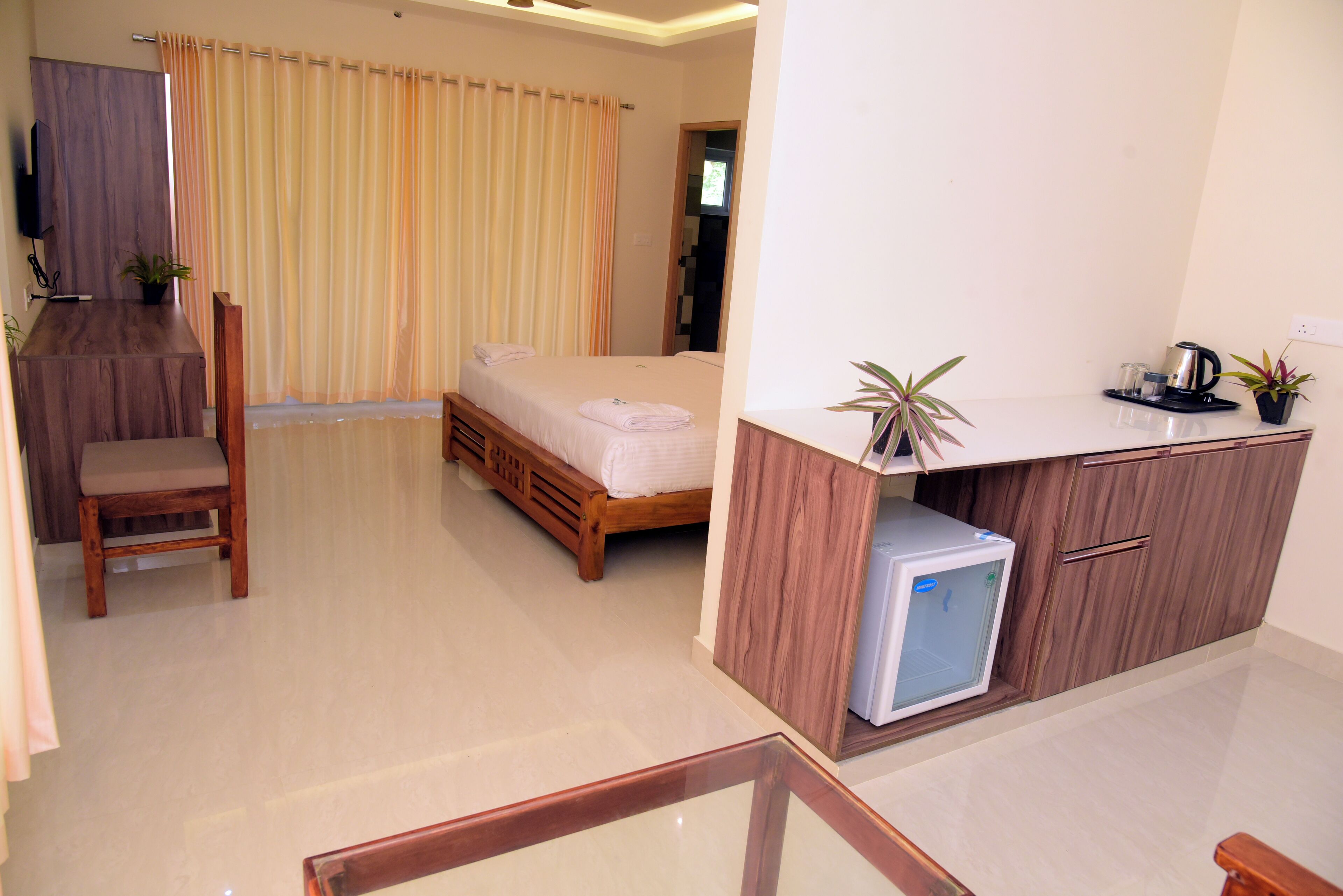 Habitación de hotel con cama, un escritorio pequeño con refrigerador, una silla y una planta en maceta.