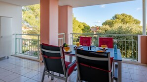 Un balcon avec deux chaises et une table, une balustrade et une vue sur les arbres et les bâtiments.