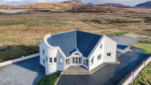 A modern house with a unique curved design, a large driveway, and a view of the surrounding landscape. - Benderloch House by Interhome (South Uist)