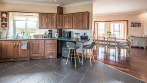 A modern kitchen with wooden cabinets, a built-in oven, and a dining area with a table and chairs. - Benderloch House by Interhome (South Uist)
