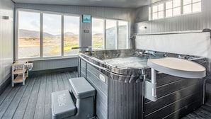 A hot tub with a wooden exterior, a bench, and a view of a mountainous landscape through large windows. - Benderloch House by Interhome (South Uist)