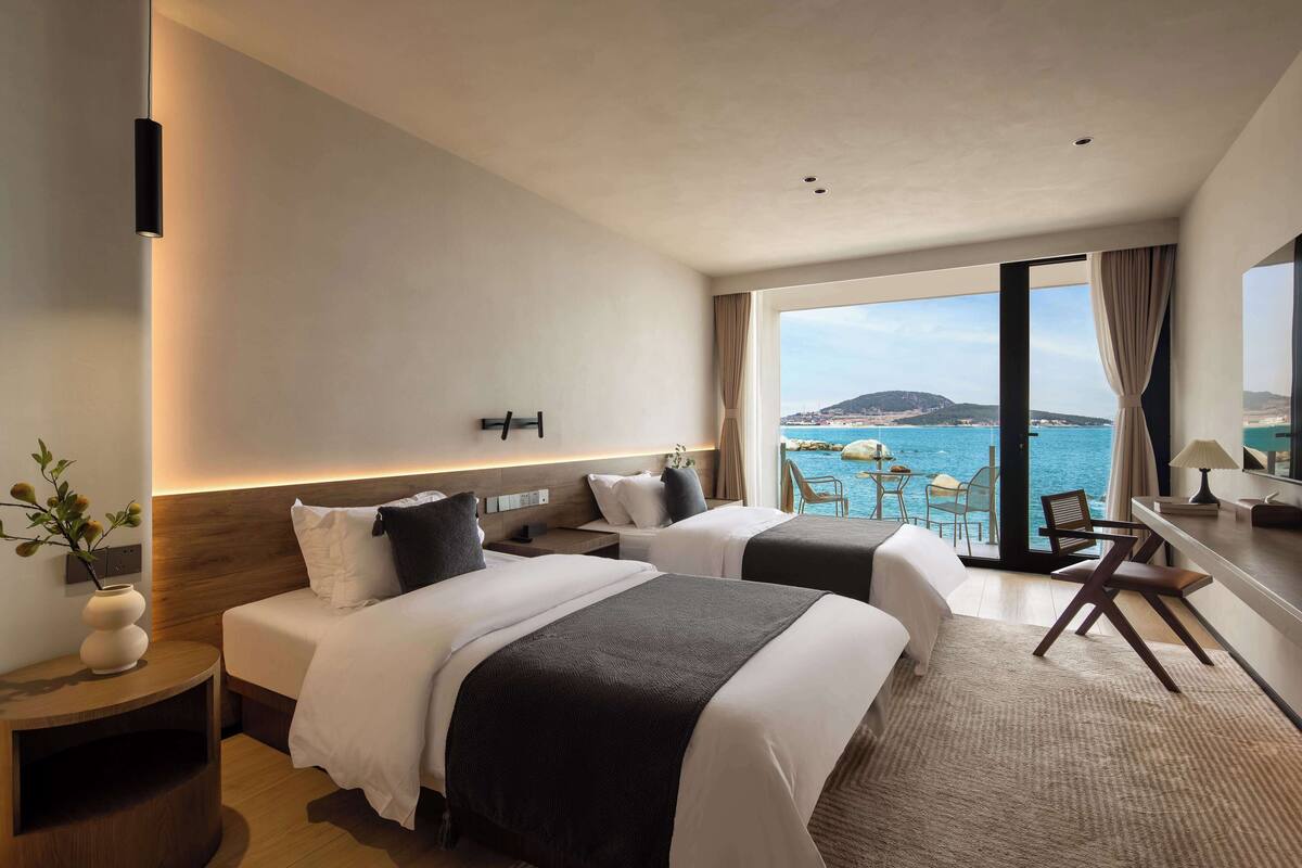 Habitación de hotel con dos camas, un escritorio y vista al mar.