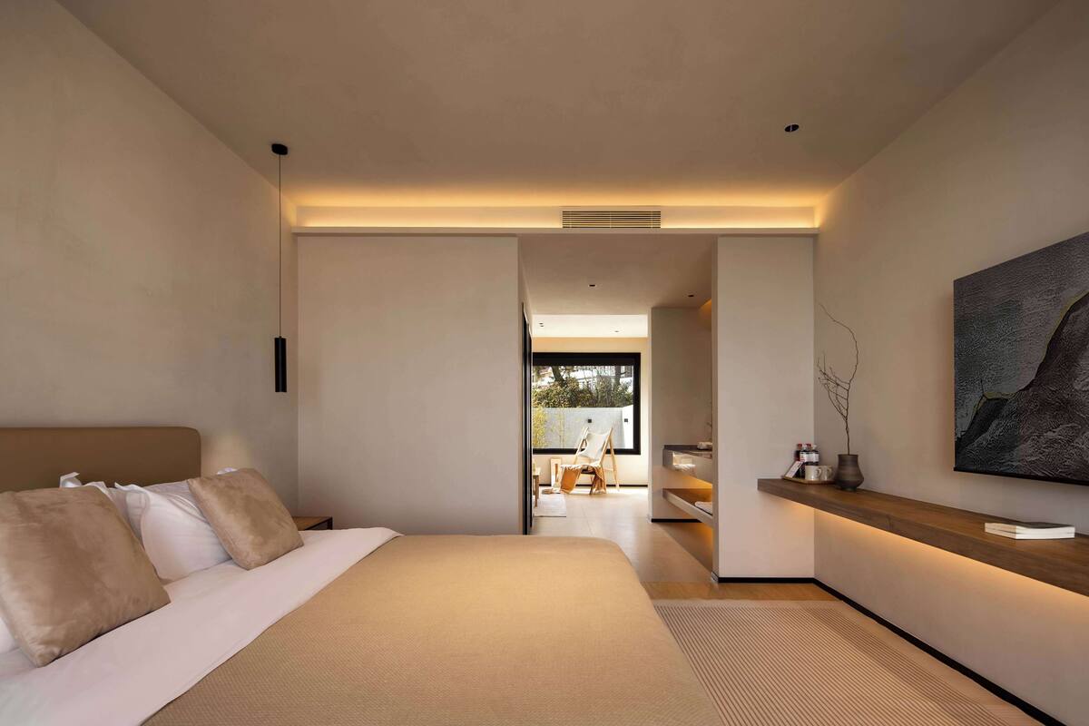 Un dormitorio moderno con una cama grande, una mesita de noche de madera, un televisor montado en la pared y vistas a un balcón.