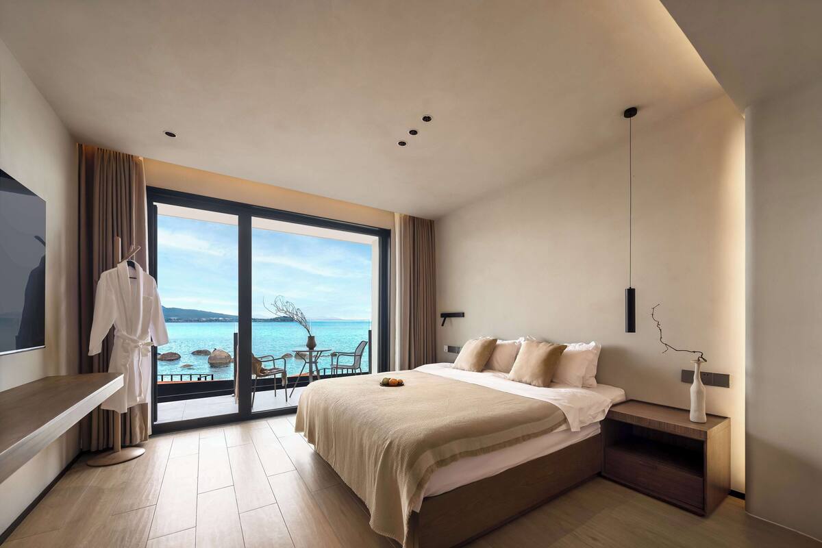 Habitación de hotel moderna con una cama grande, una mesita de noche, un televisor y vistas al mar.