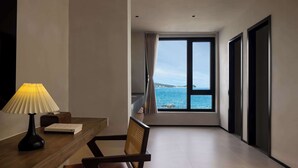 Habitación de hotel con vista al mar, una mesa de madera con una lámpara, una silla y un sofá.