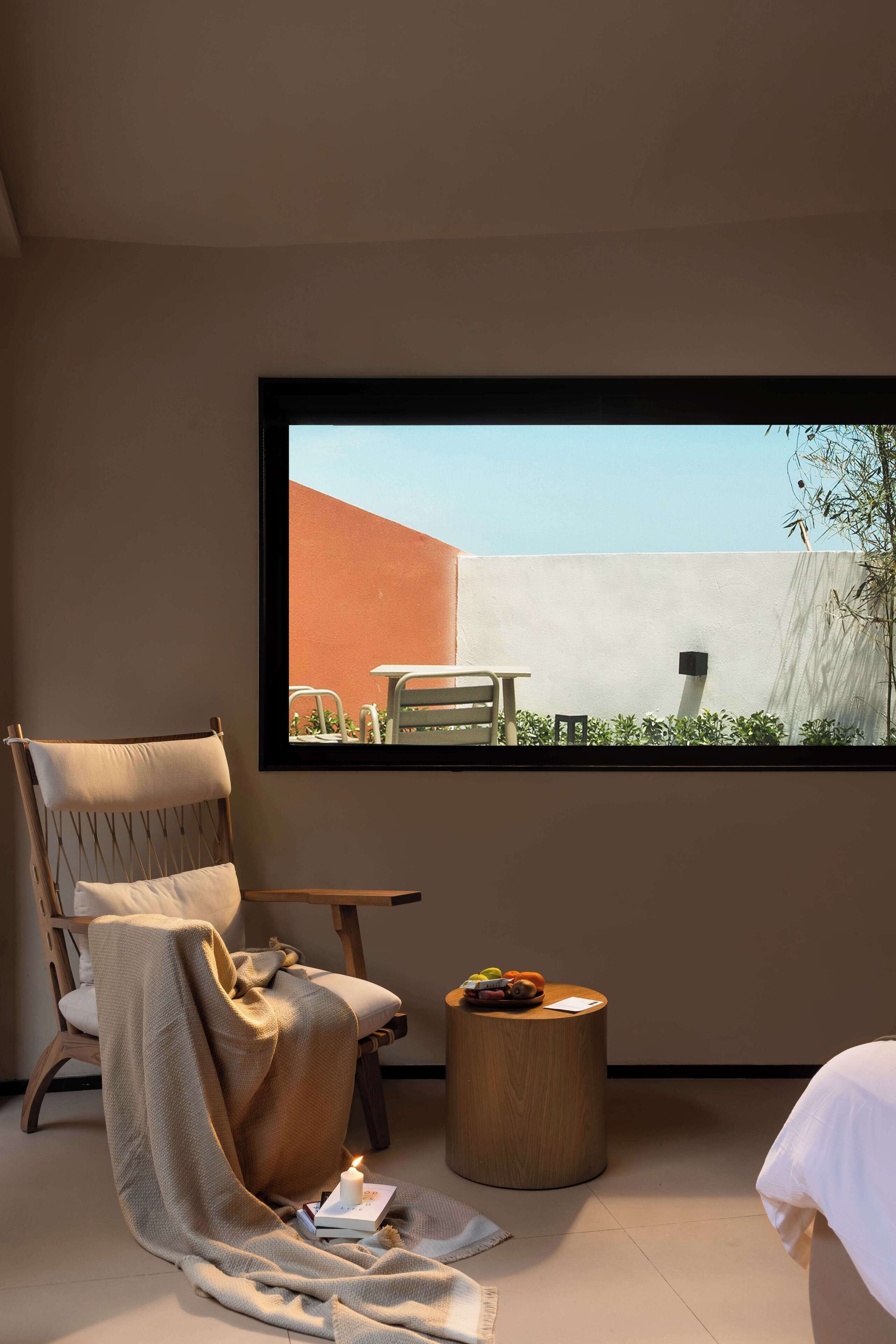 Una habitación acogedora con un ventanal grande, una silla de madera, una pequeña mesa redonda de madera y una cama blanca.