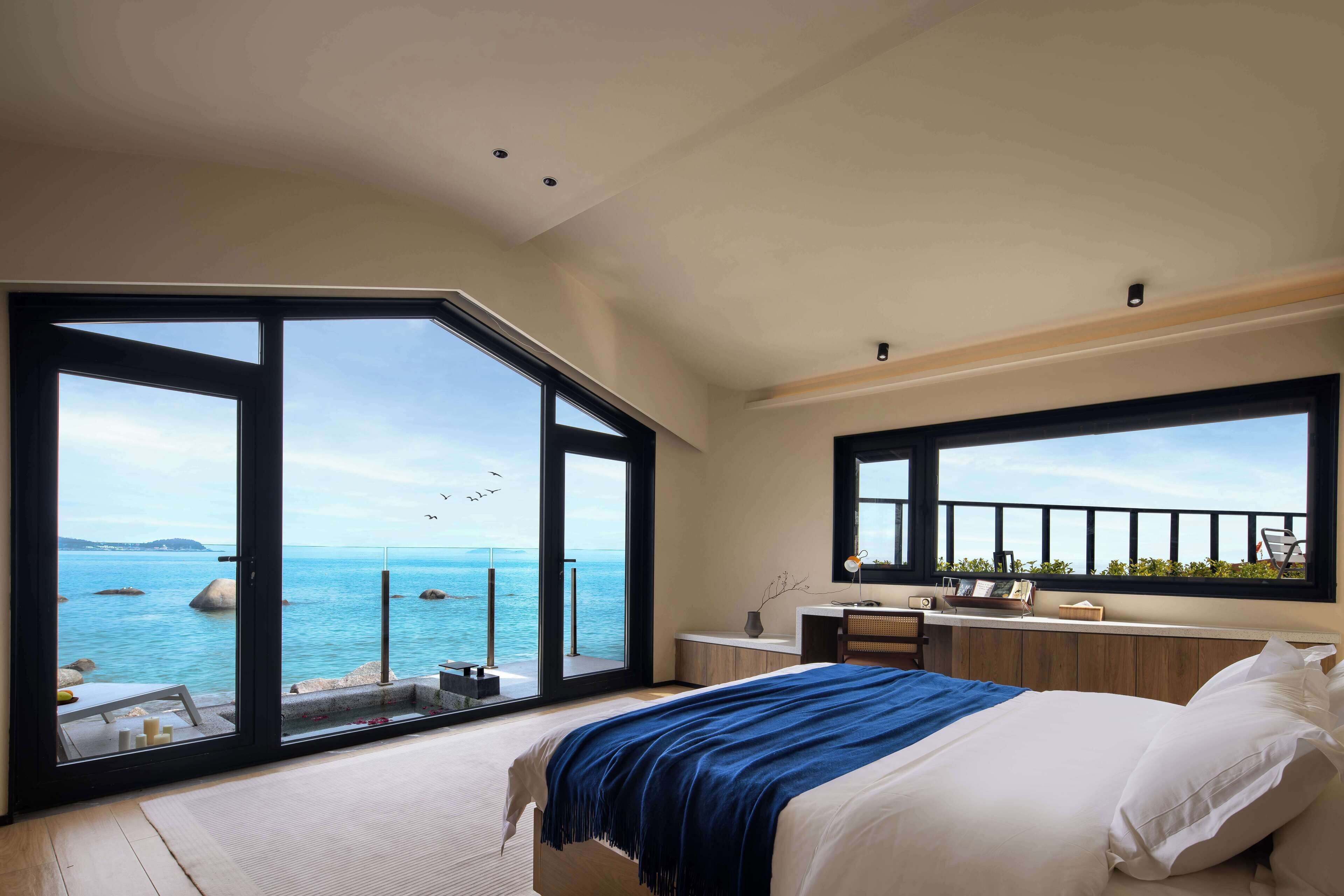 A bedroom with a large bed, a desk, and a view of the sea.