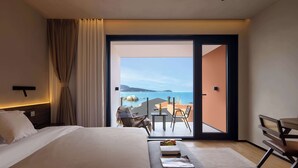 Una habitación de hotel con cama, sofá, zona de comedor con mesa y sillas, y balcón con vistas al mar.