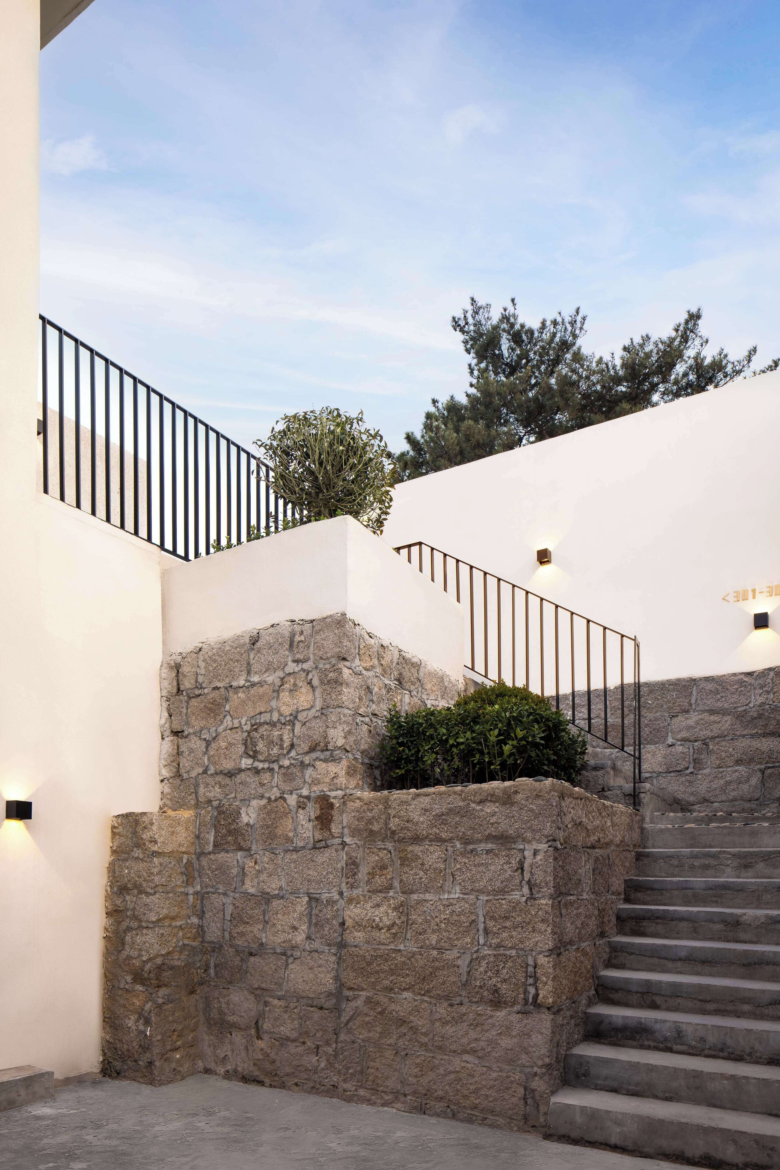 Una escalera con paredes de piedra y barandales de metal que conduce a un edificio blanco.