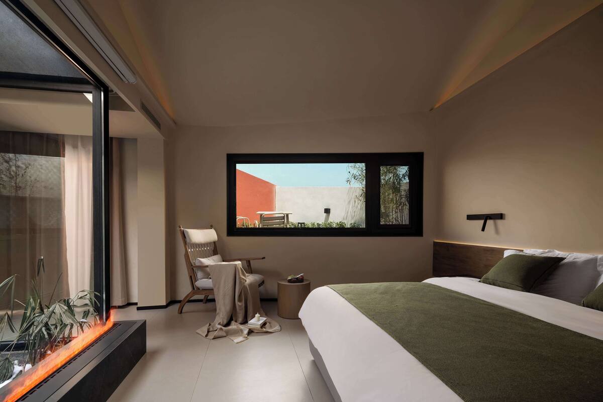 Un dormitorio moderno con cama, una silla, una mesita y una chimenea.