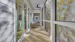 Un porche cubierto con ventilador de techo, puertas correderas de vidrio y vista a una casa y árboles.