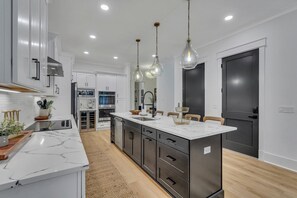 A modern kitchen with white cabinetry, a marble countertop, and pendant lighting.