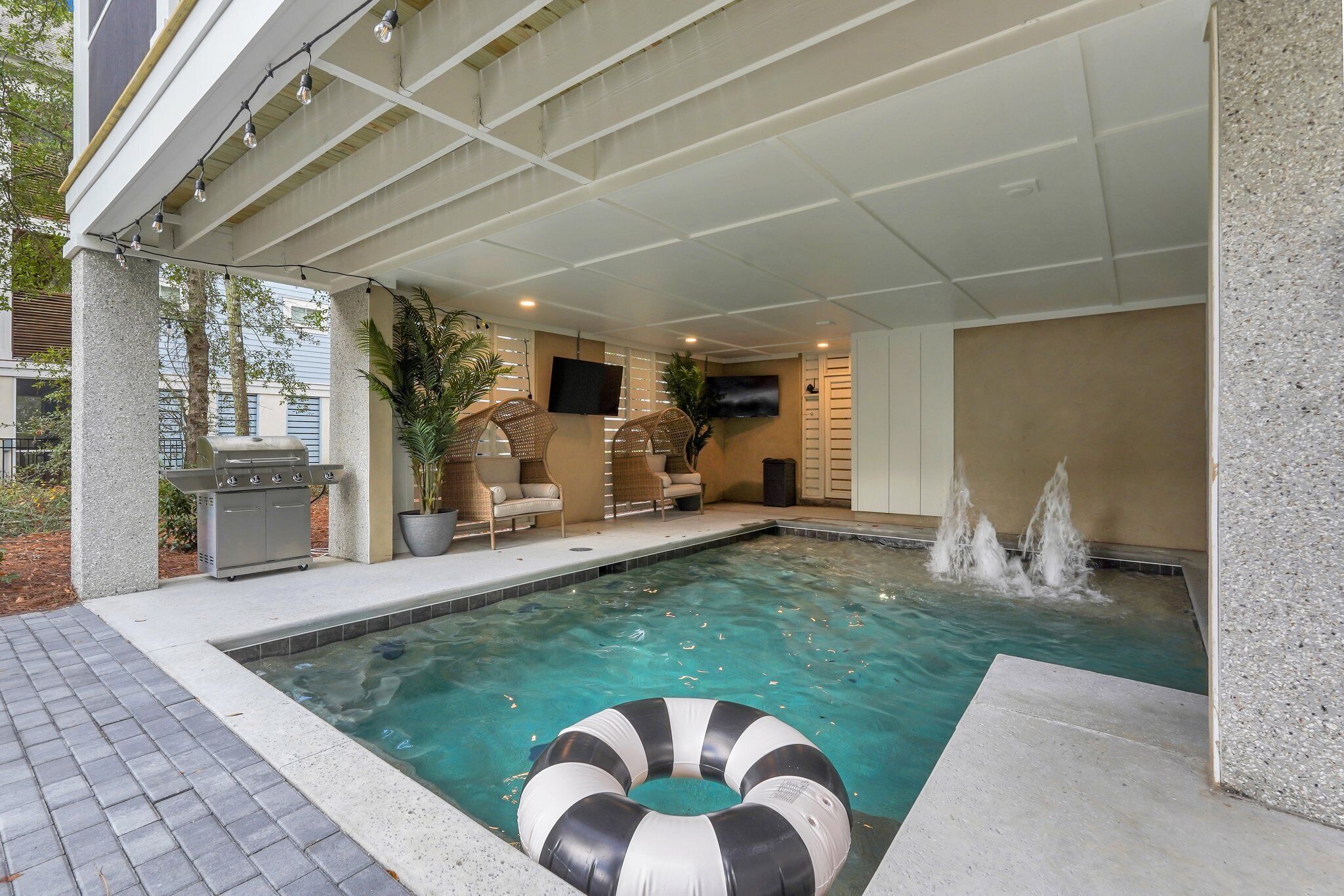 A swimming pool with a lounge area, a grill, and a flat-screen TV.
