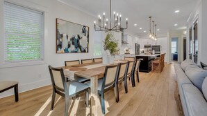 Una cocina moderna con armarios blancos, una isla central y una zona de comedor con mesa y sillas de madera.