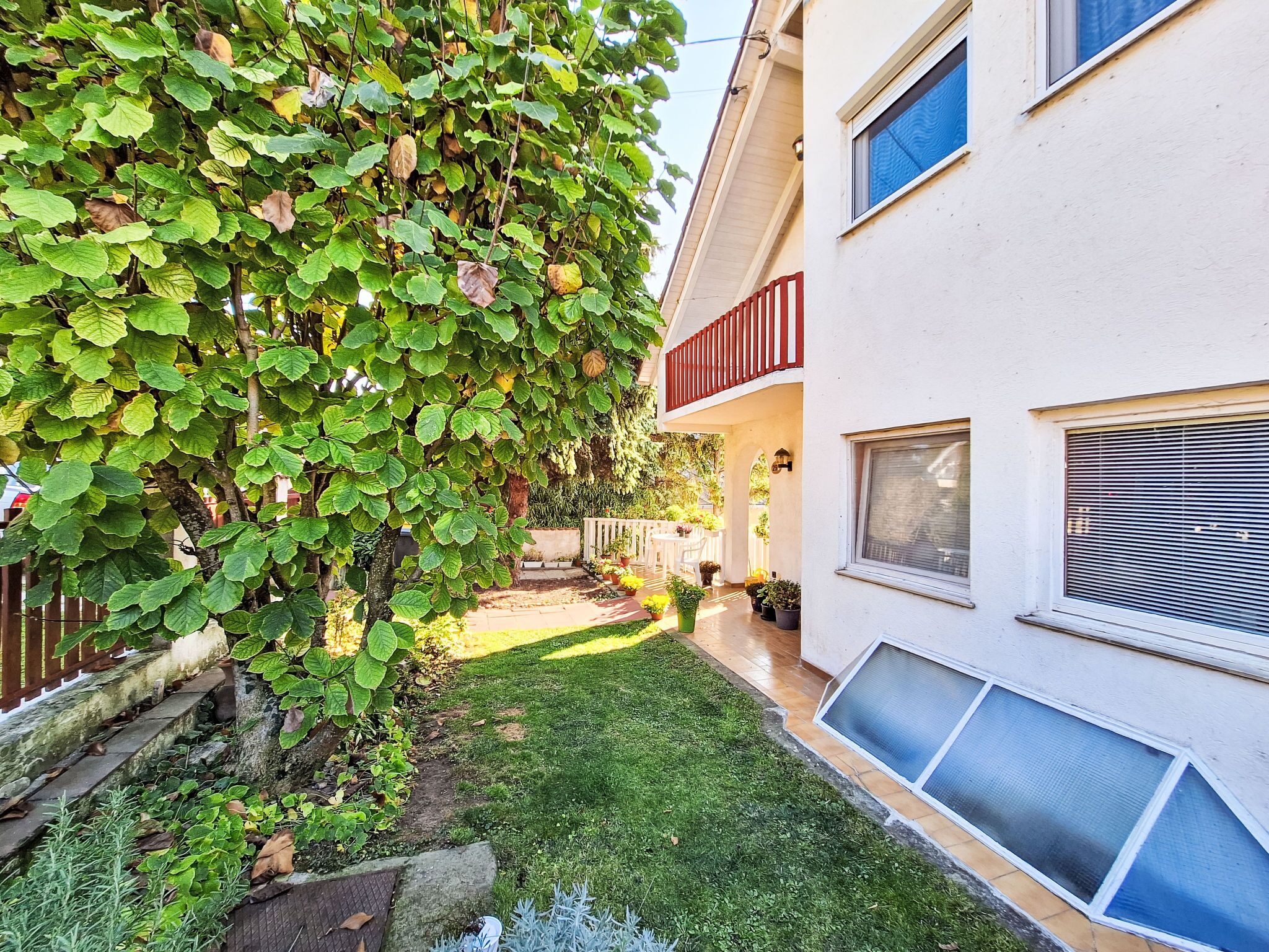 A residential building with a small garden, a red balcony, and a white exterior wall.