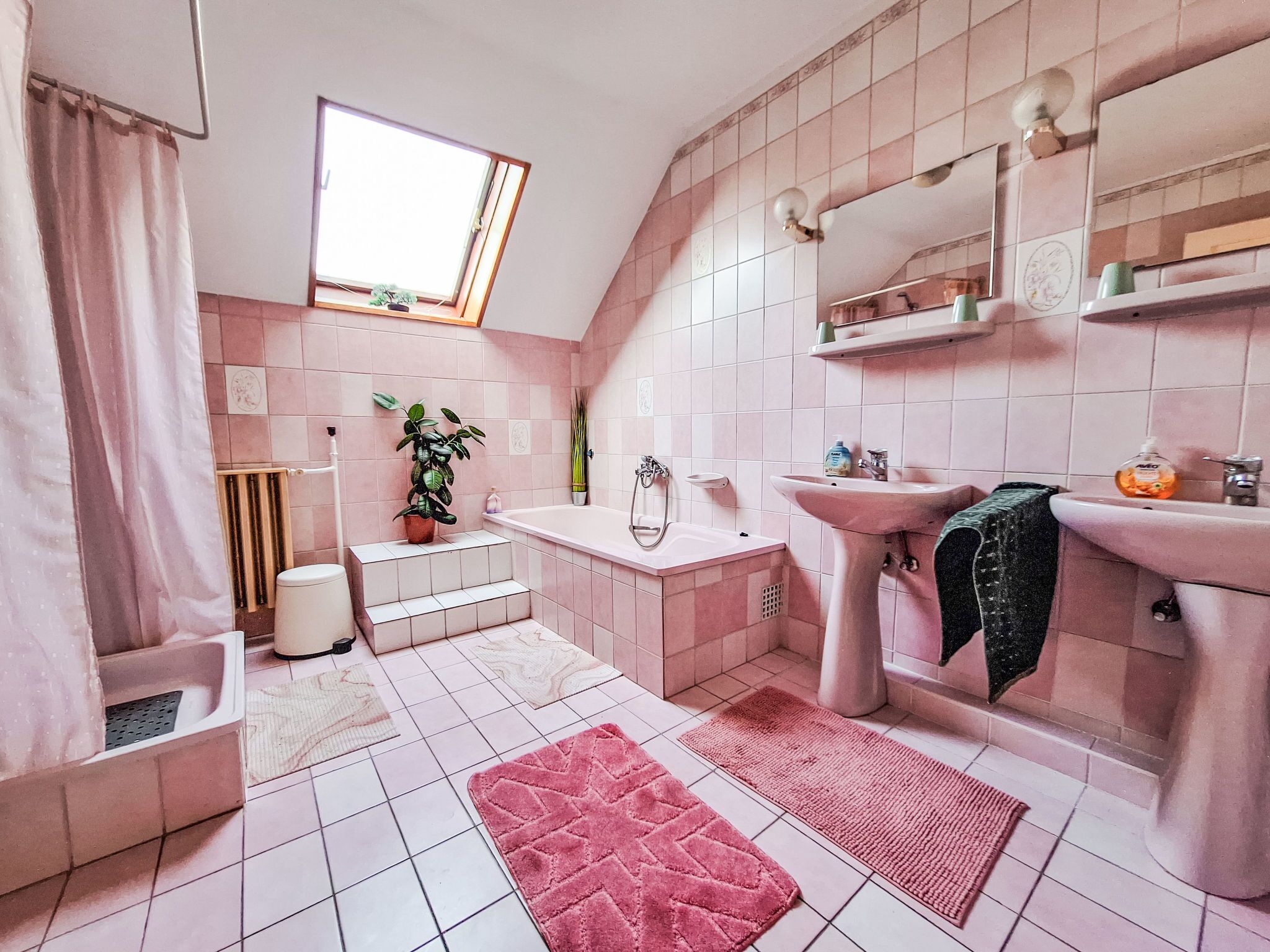 A bathroom with pink tiles, a bathtub, a sink, a mirror, and a window.