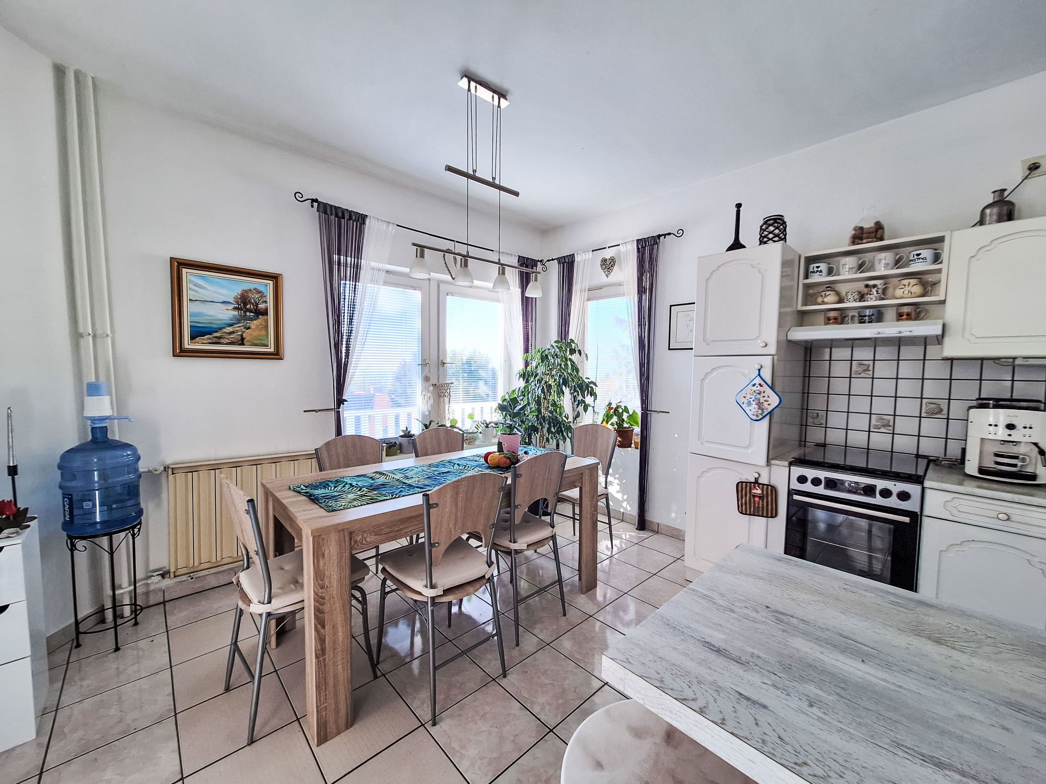 A compact kitchen with a dining area, featuring a stove, cabinets, and a water dispenser.