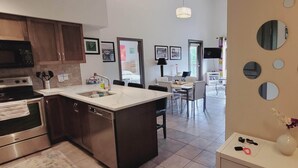 Una cocina moderna con una isla central, electrodomésticos de acero inoxidable y una zona de comedor con una mesa y sillas blancas.