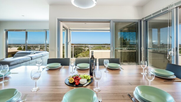 A dining area with a wooden table set for six, a bottle of wine, and a fruit platter. - 94 Aldebaran Rd.  (Ocean Grove)