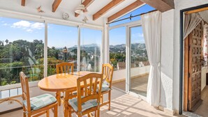 A spacious balcony with a wooden table and chairs, large windows offering a view of a hilly landscape. - Casita Blanca by Interhome (Moraira)