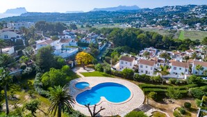 A residential area with a large circular swimming pool surrounded by lush greenery and white houses with red-tiled roofs. - Casita Blanca by Interhome (Moraira)