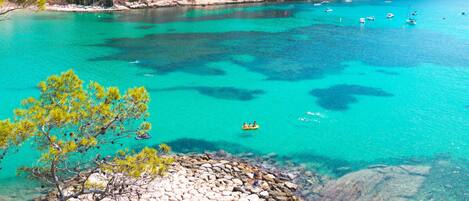 A coastal town with buildings along the shoreline, clear turquoise waters, and rocky terrain.