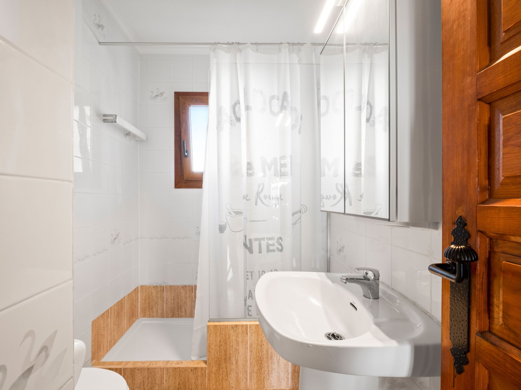 A bathroom with a white sink, wooden vanity, and a mirror.