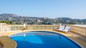 A swimming pool with two sun loungers, a balustrade, and a view of a mountainous landscape.