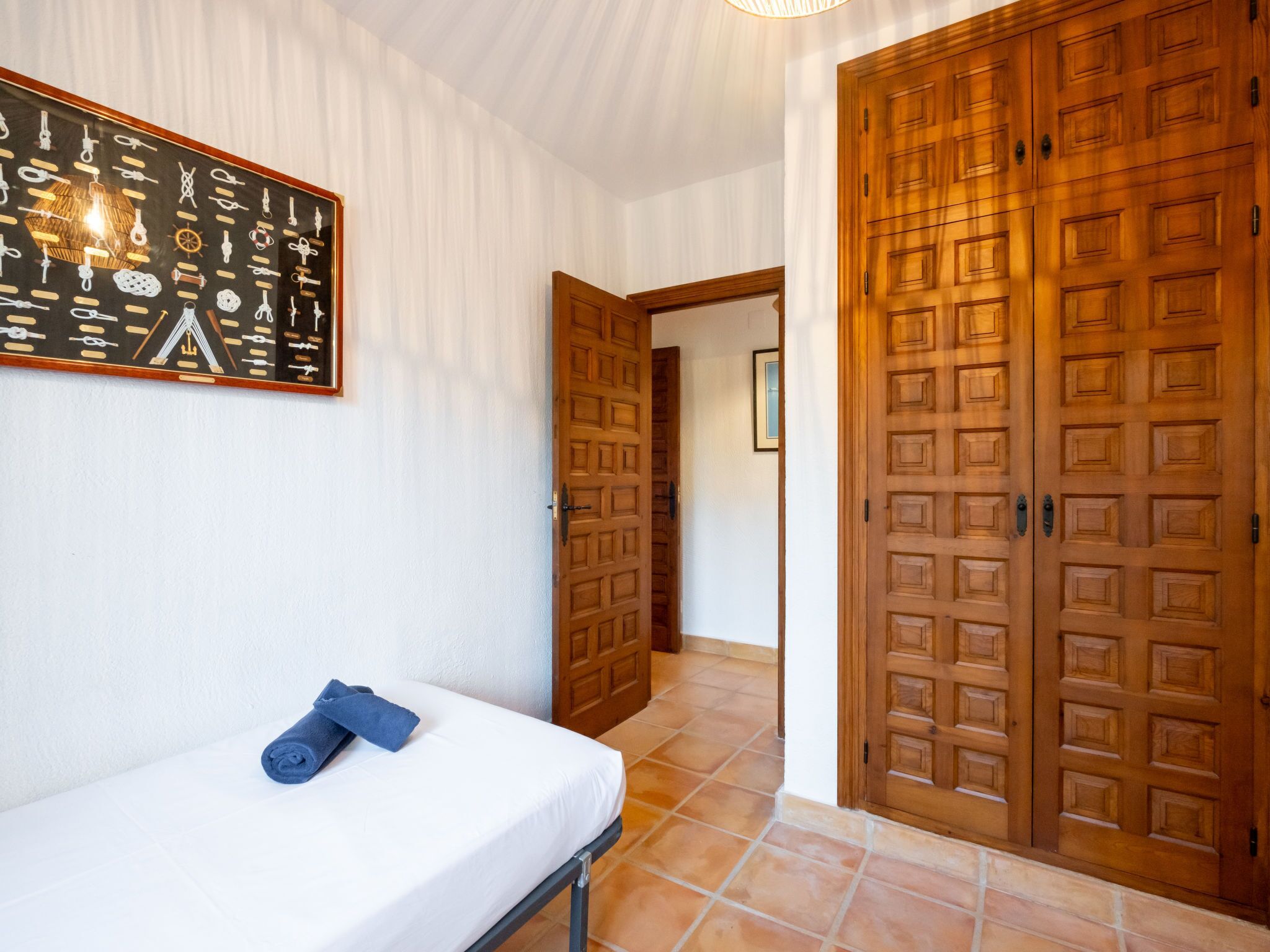 A hotel room with a bed, a towel, a wooden door, and a wall with a framed picture.