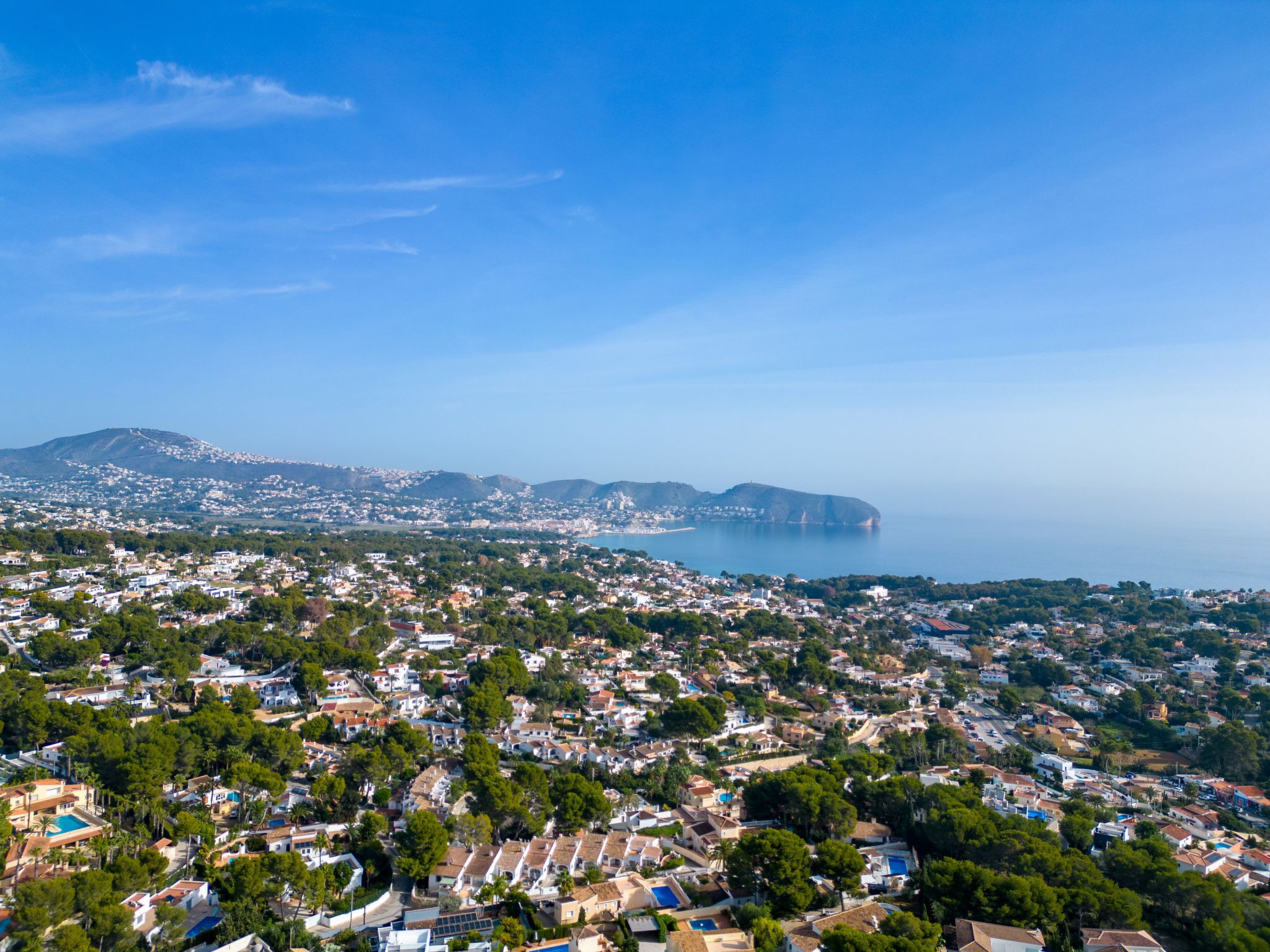 A coastal town with dense housing, a mountain in the background, and a clear view of the sea.