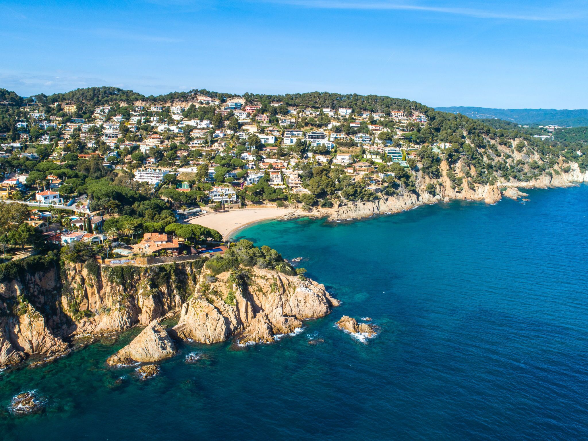 An aerial view of a coastal town with a beach, rocky coastline, and residential buildings.