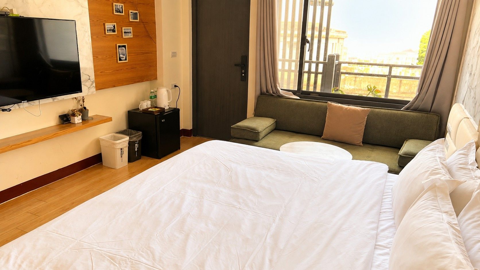 A hotel room with a bed, a TV, a small seating area, and a window with curtains.