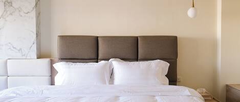 Una cama bien hecha con un cabecero, una mesita de noche blanca y una pared de mármol.