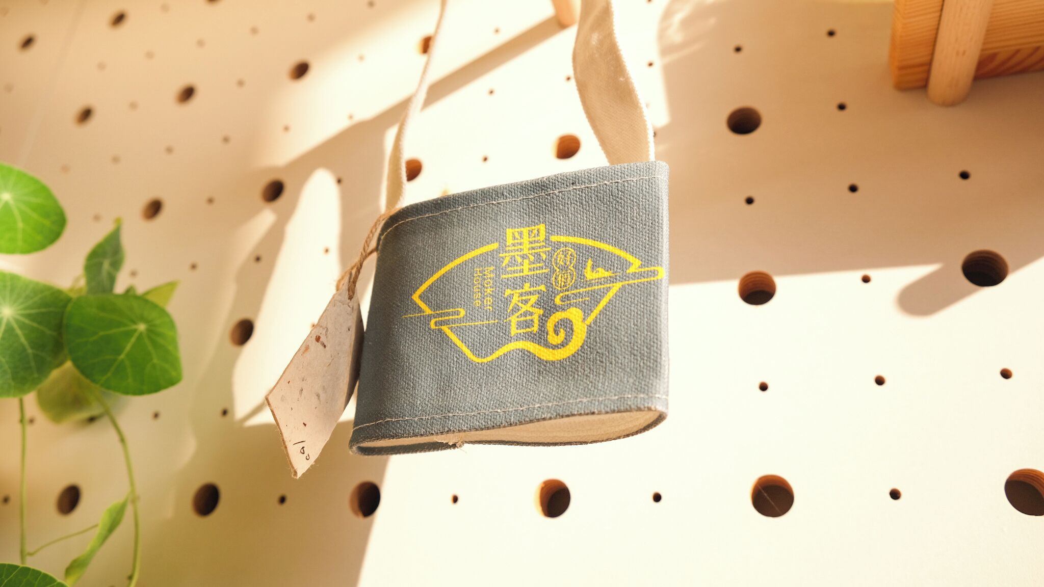 A small, dark-colored bag with a yellow emblem, hanging on a pegboard with multiple holes.
