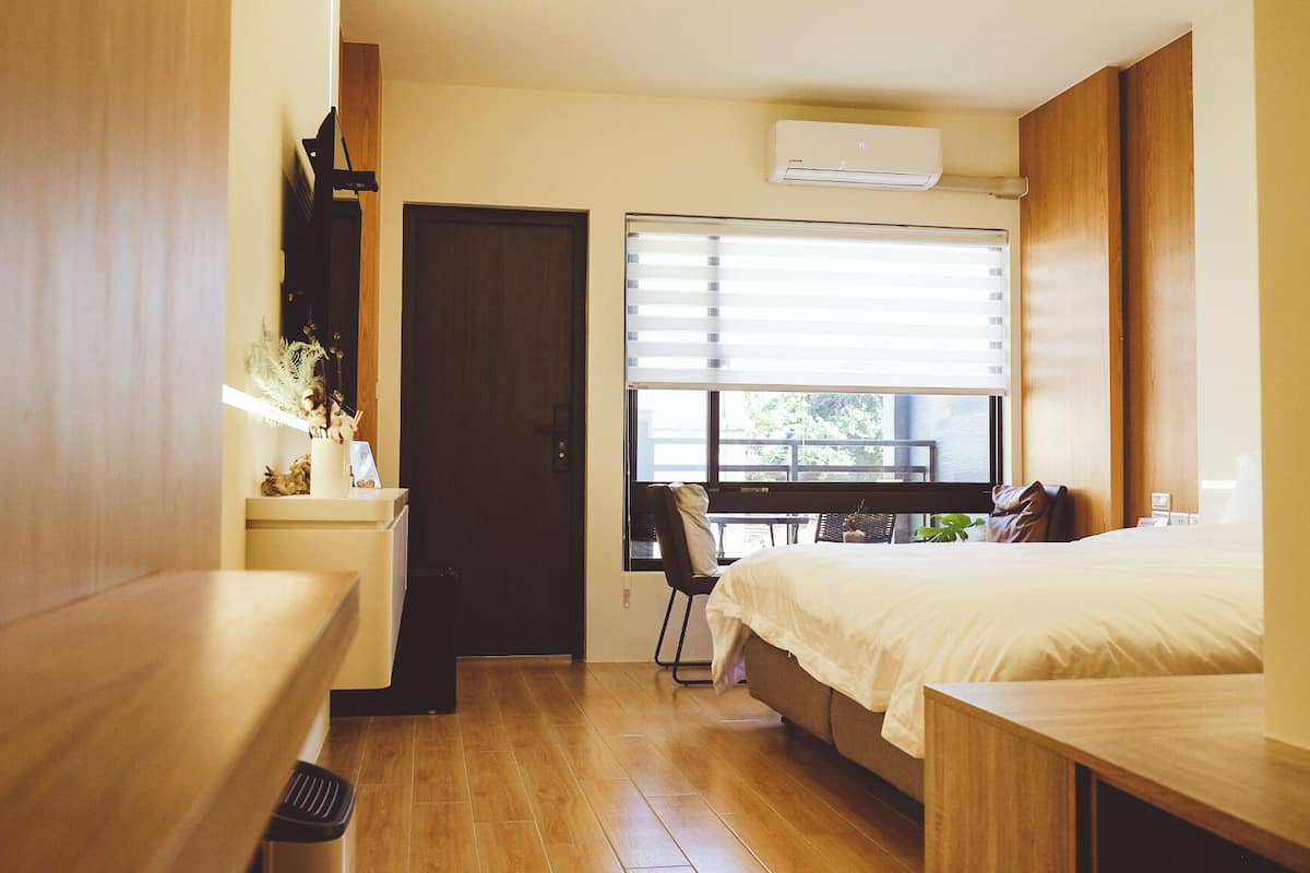 A compact hotel room with a bed, a desk, a chair, and a window with blinds.
