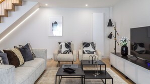Een moderne woonkamer met een trap, een zithoek, een salontafel, een televisie en een vloerlamp.